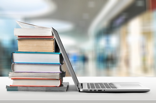 Stack of books with laptop on wooden table